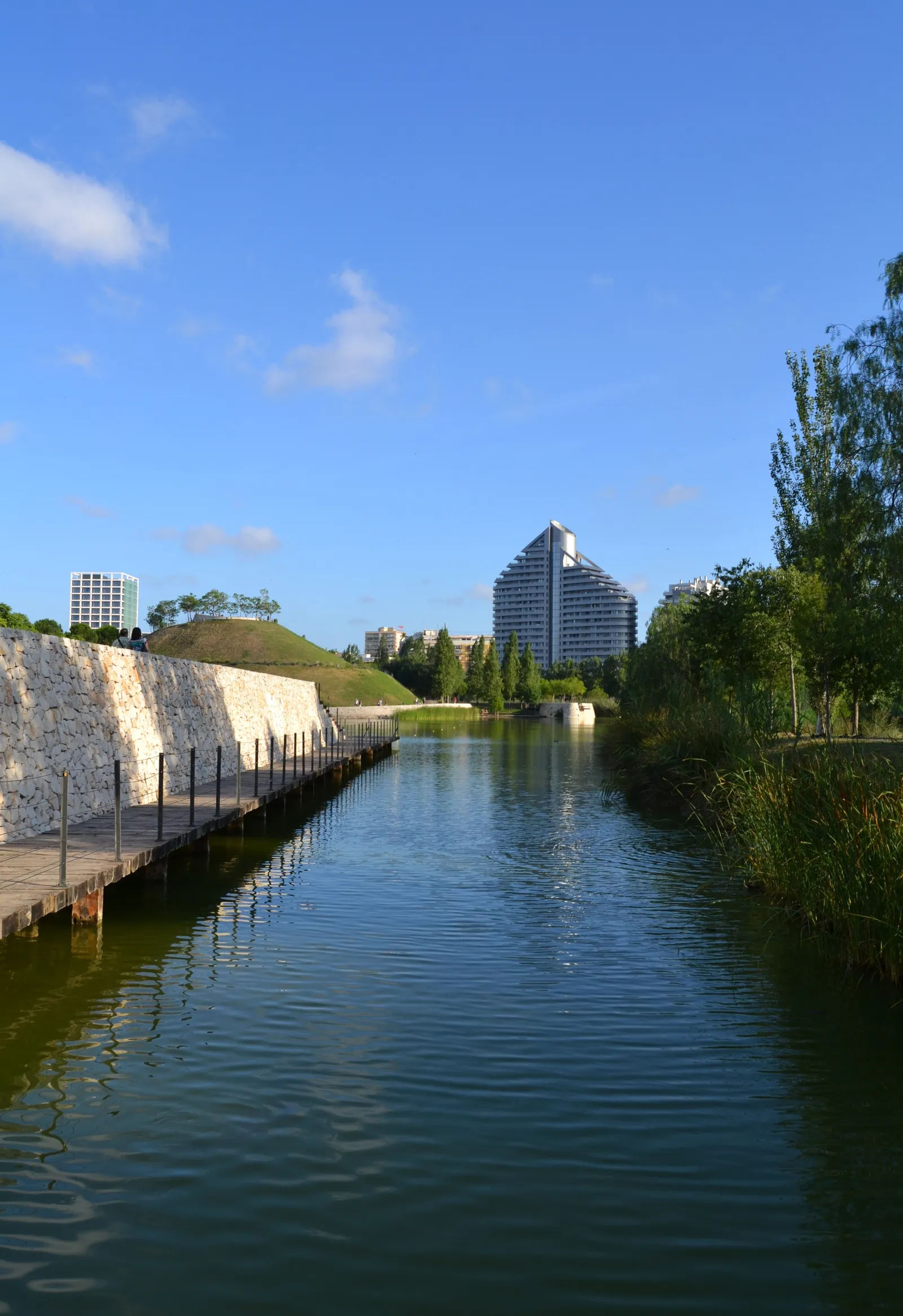 Water channel in Parc de Capcalera with banks of grass and trees on both sides.