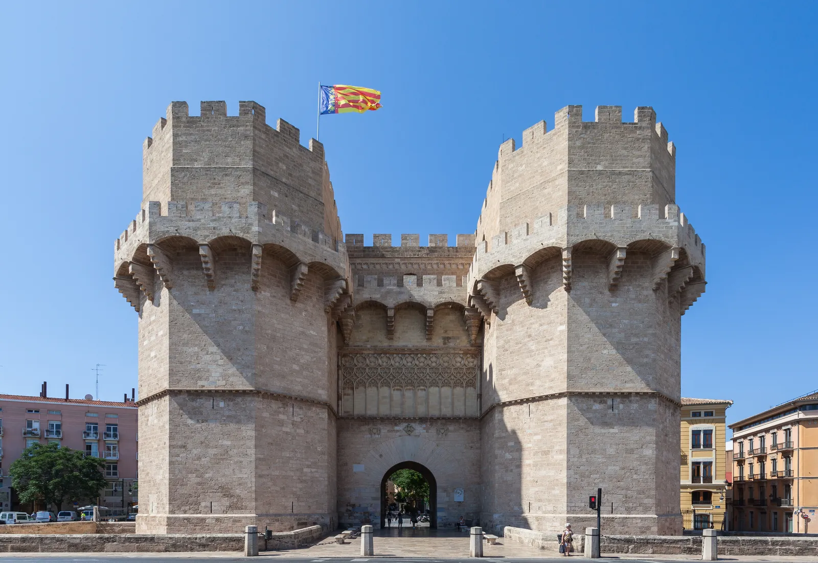 The two crenellated stone towers of the Torres de Serranos city gate under a blue sky.