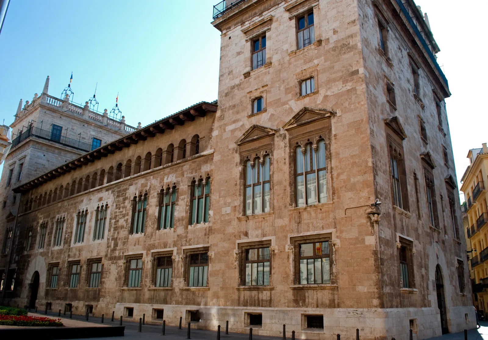 Stone facade of a historic palace with tall arched windows and a tower, seen from the street