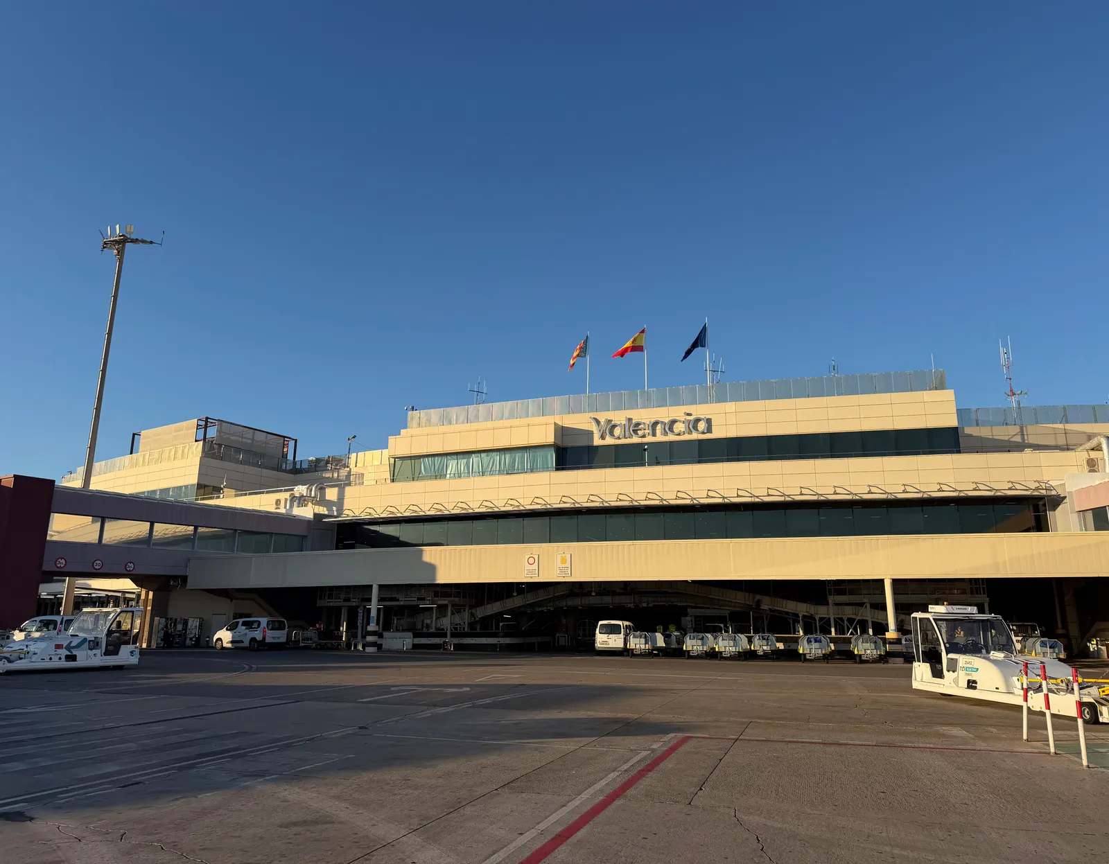 Front of the Valencia airport terminal building with the airport name on the roof and service vehicles in front