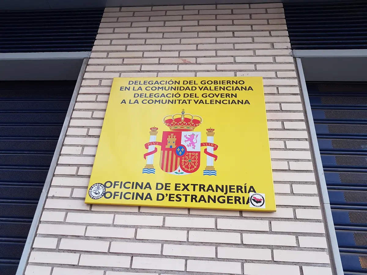 Yellow government sign reading Oficina de Extranjeria on a white brick wall