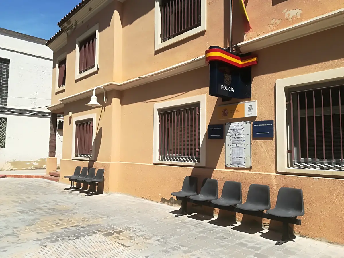 Police station facade with a flag over the door and a row of seats on the pavement