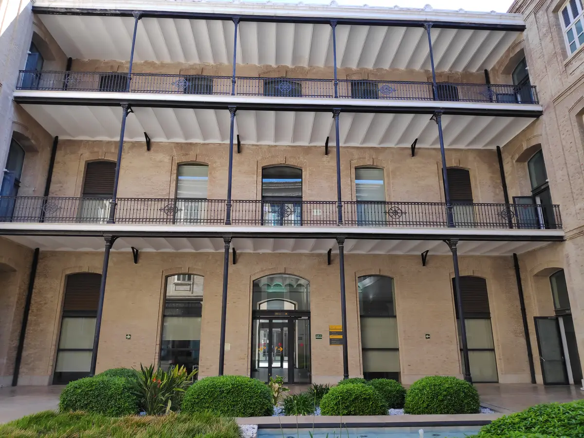 Glass entrance with balconies and hedges in front of a brick building