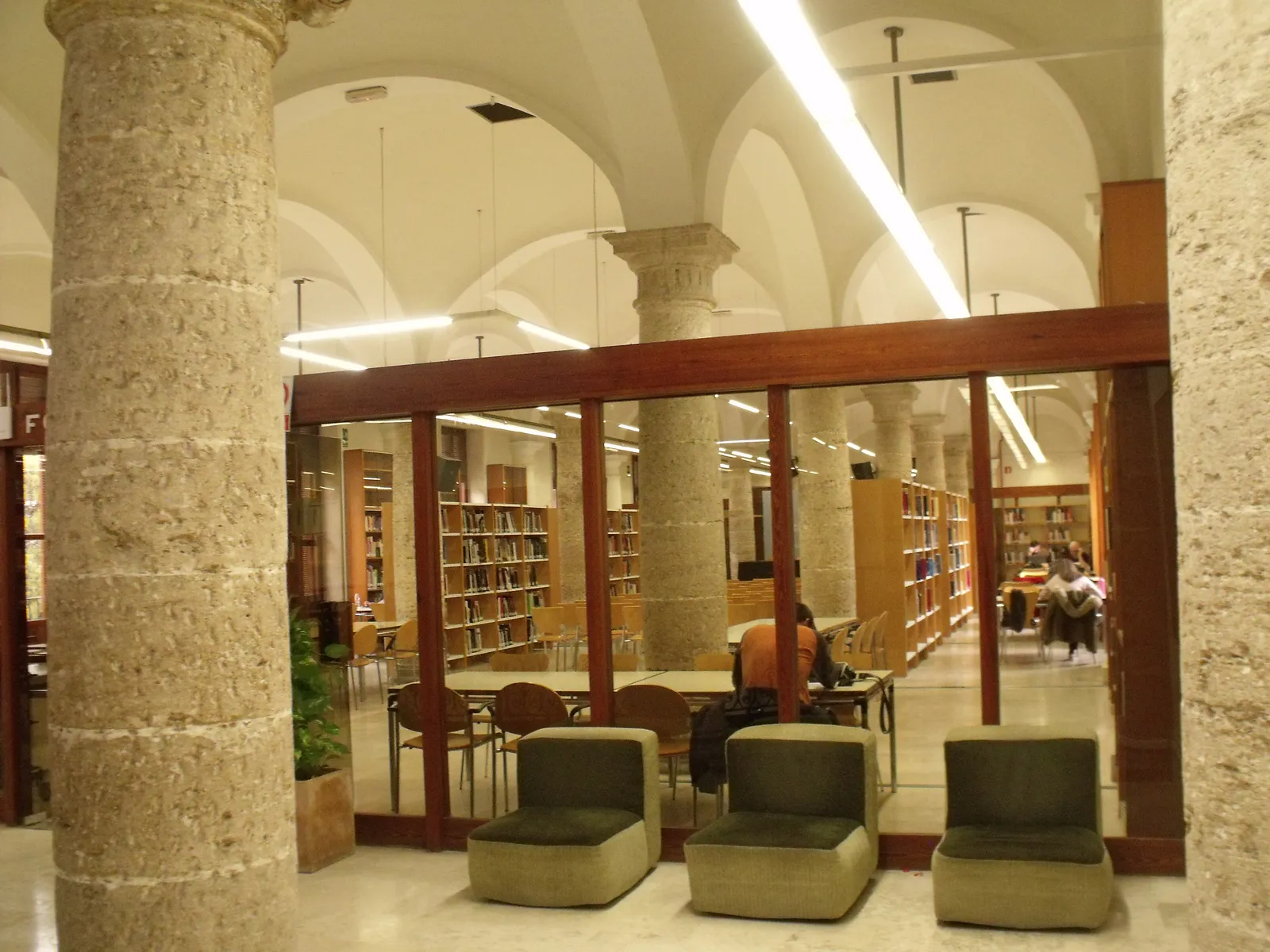 Reading room of a municipal library in Valencia with armchairs and shelves behind glass.