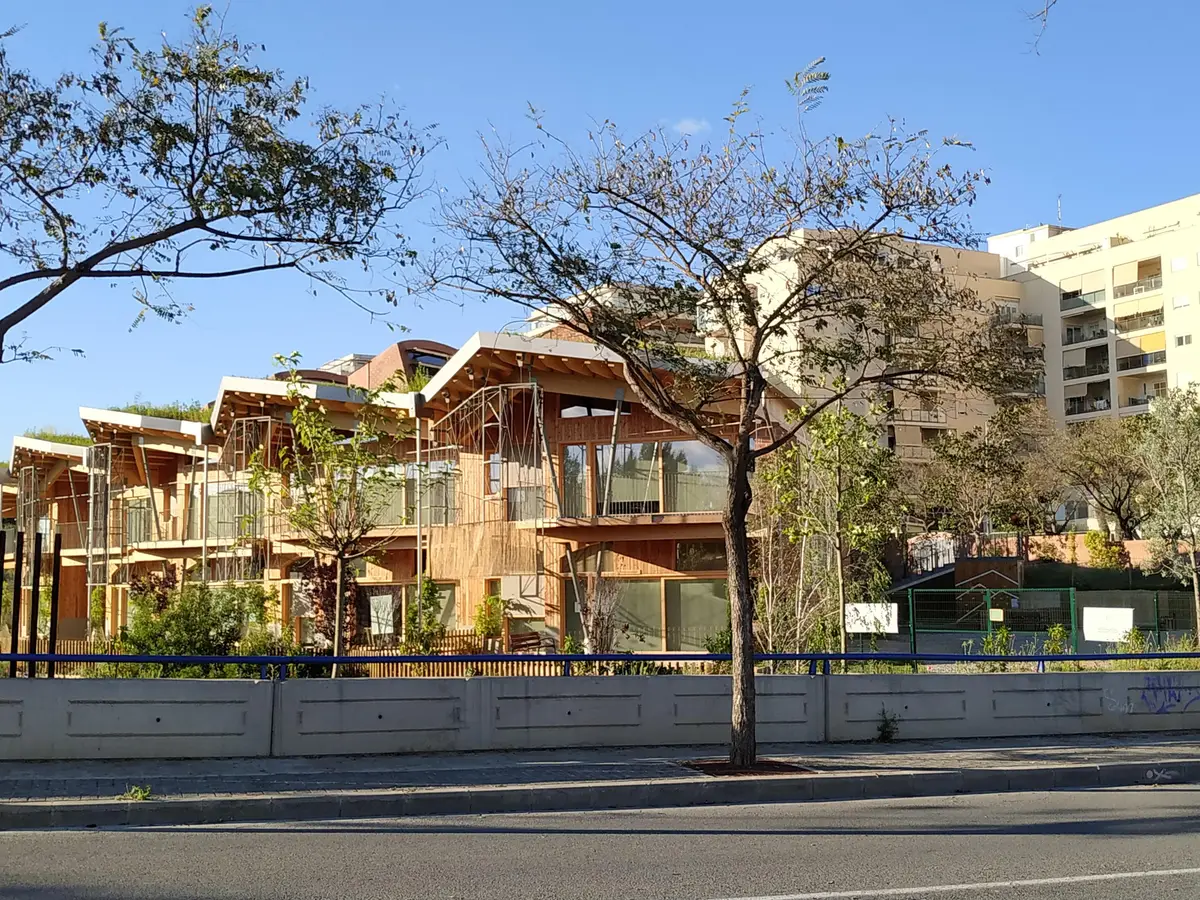Wooden and brick school buildings with terraces behind trees, seen from the street