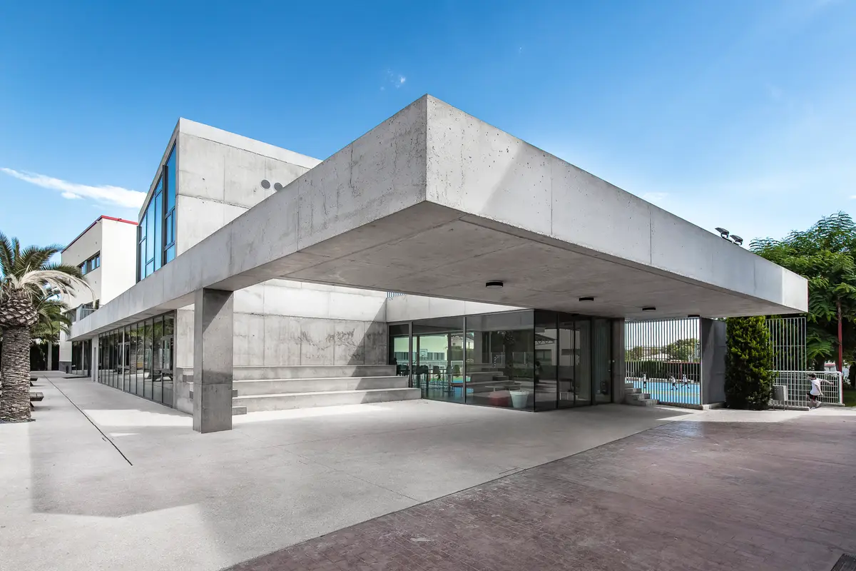Concrete school building with a wide flat roof and glass walls beside a sports court