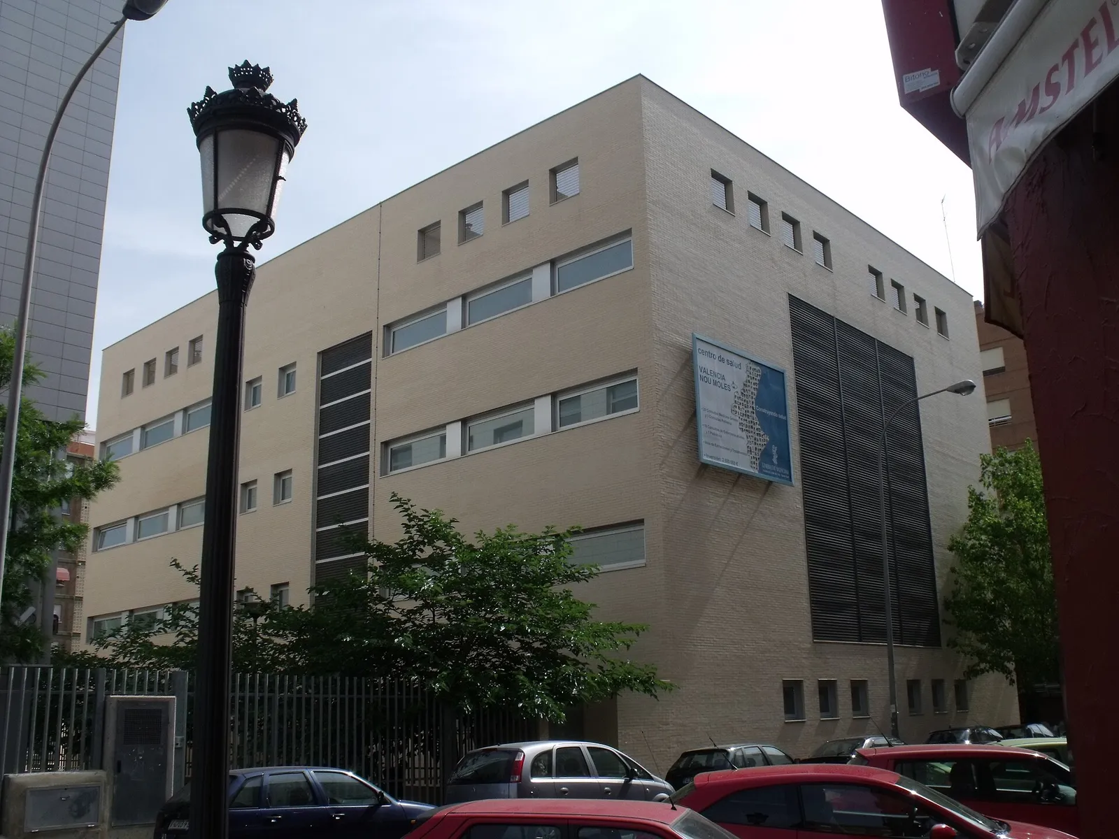 Beige health centre building on a city street with a street lamp and parked cars
