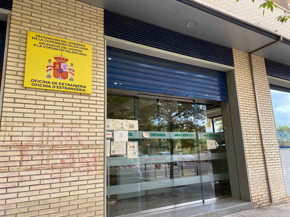 Entrance of the foreigners office in Valencia with a yellow government sign beside the glass door.