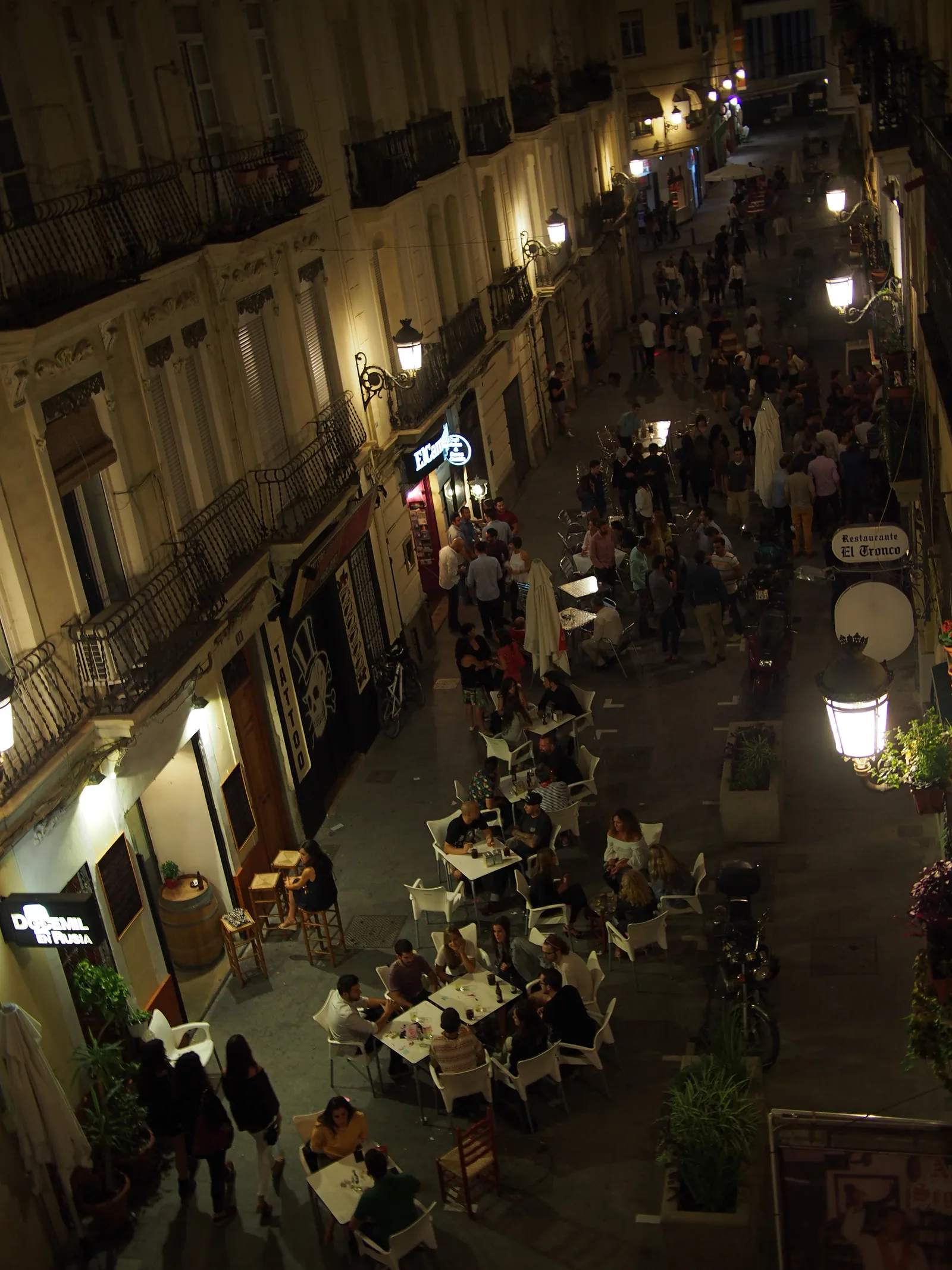 Pedestrian street in Russafa at night, seen from above, with restaurant terraces lit along both sides.