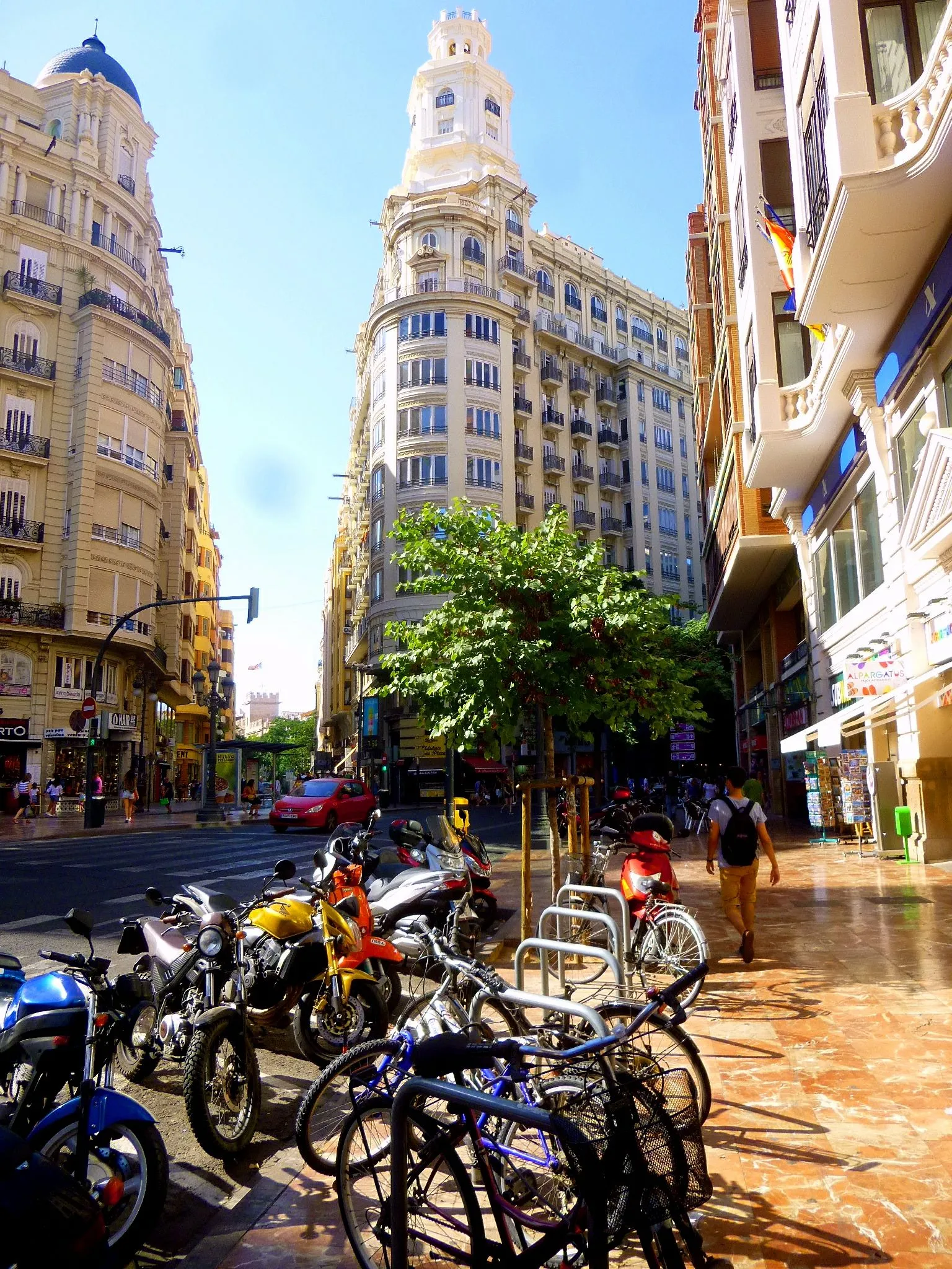 Tall buildings and parked bicycles on a sunny street beside the Plaza del Ayuntamiento.