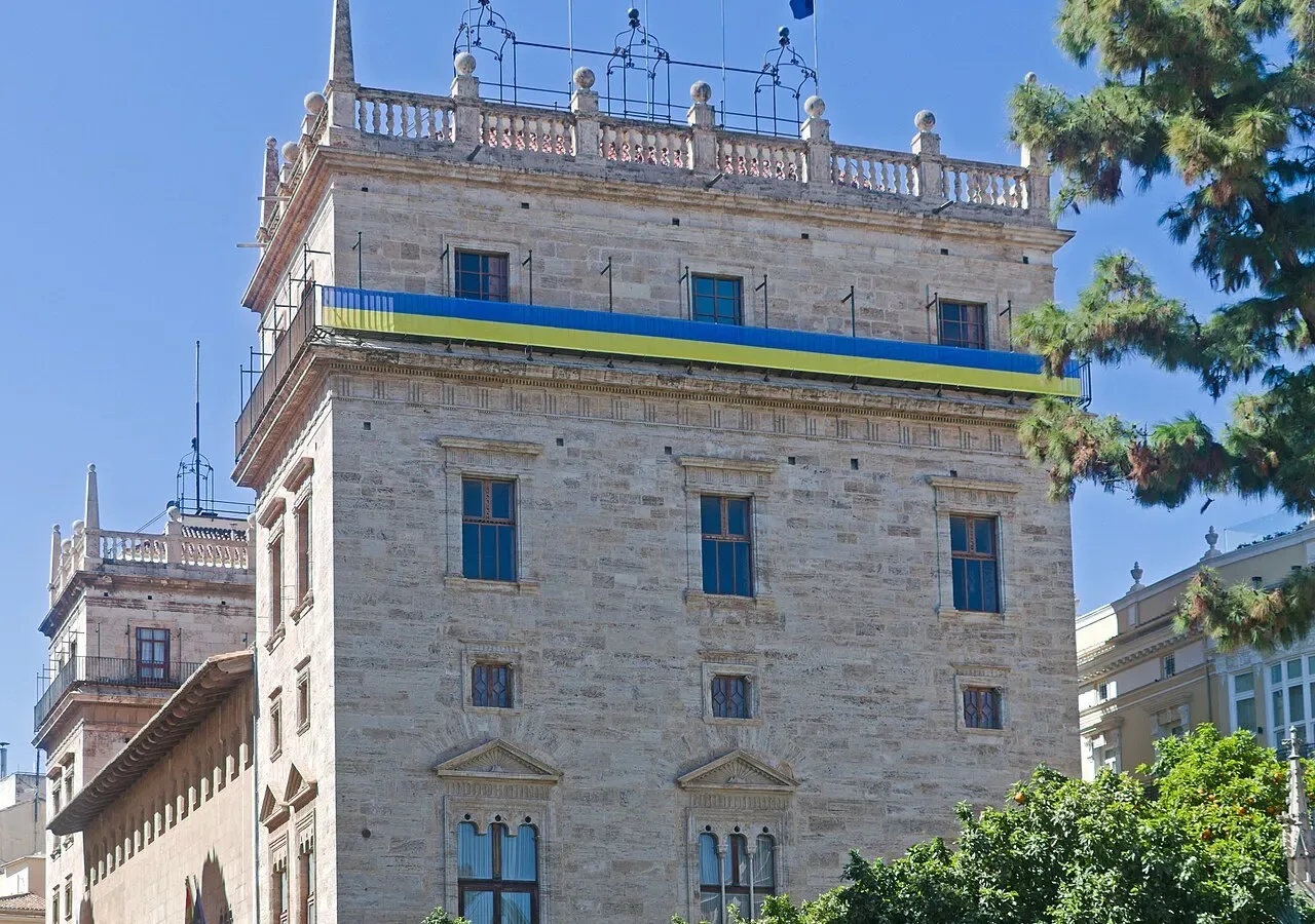 Historic palace with a stone tower and rows of arched windows under a blue sky.