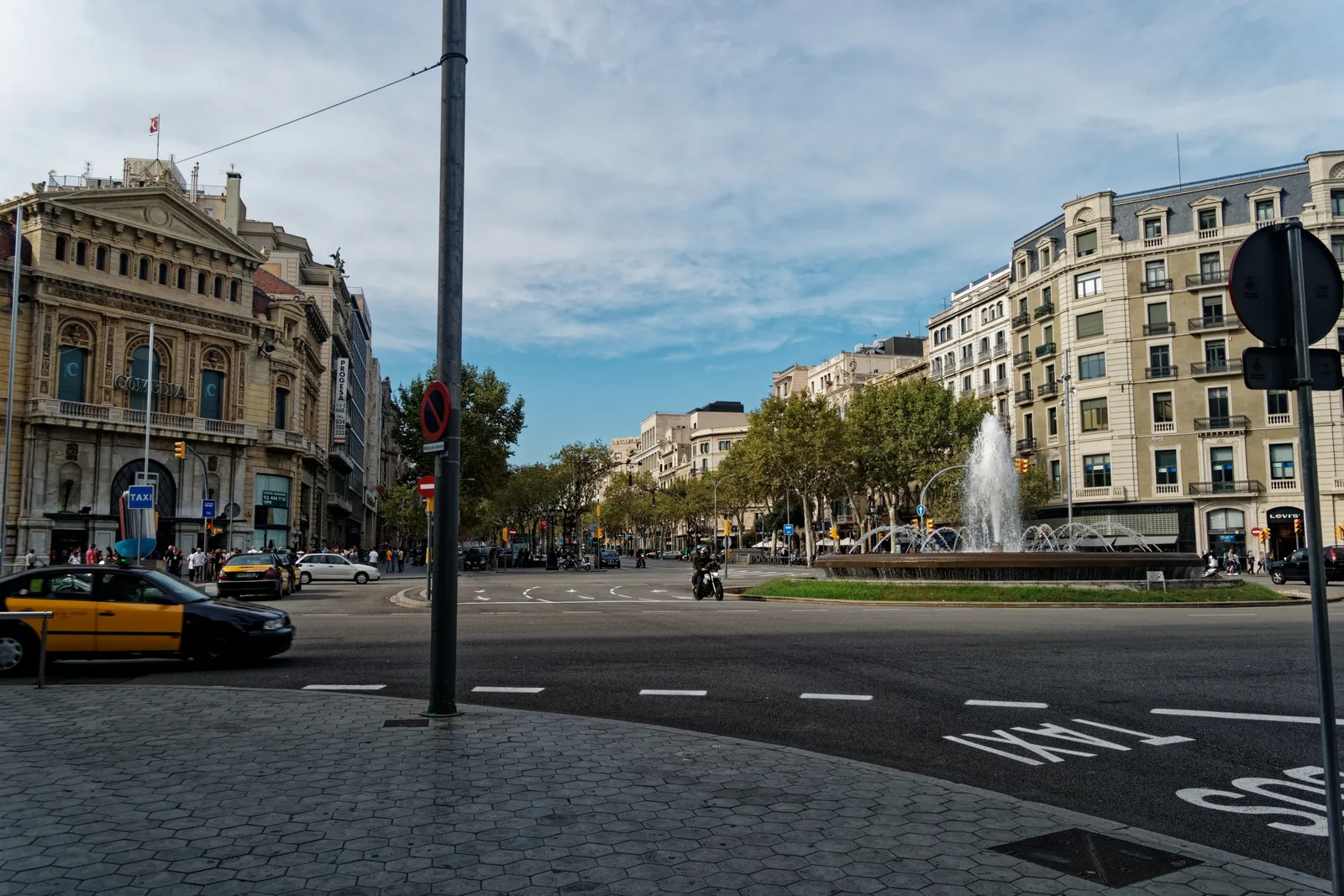 A broad Barcelona avenue with a fountain, a taxi and stone apartment buildings
